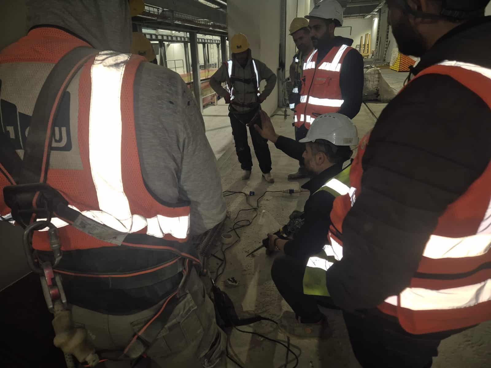 קבוצת עובדים עם ציוד מגן באתר בנייה, מקשיבים להדרכה בטיחותית.