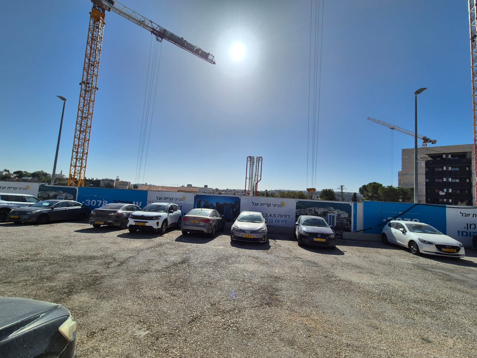 אתר בנייה עם מנופים ורכבים חונים, בשמש בהירה.